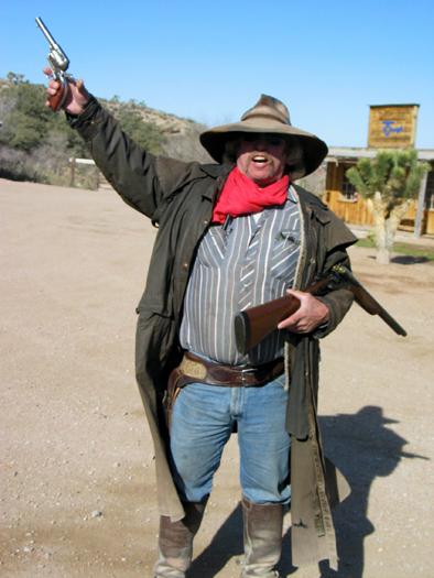 master_1924.jpg - This is the introduction to the shootout reenactment.  When we first arrived, Billy walked around a fence carrying the shotgun shown here, with the action closed.  Since I wasn't armed, the only thing I could do was throw up my hands.  We've never been greeted anywhere by a guy in a duster carrying a sawed off.